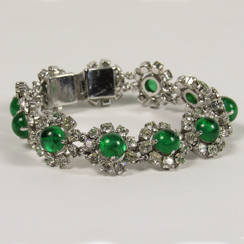 Costume jewelry at its finest, this 1973 Christian Dior bracelet features linked florets with green cabachon stones surrounded by clear glass diamond petals in a silver tone setting. Measures: Length 7 inches.